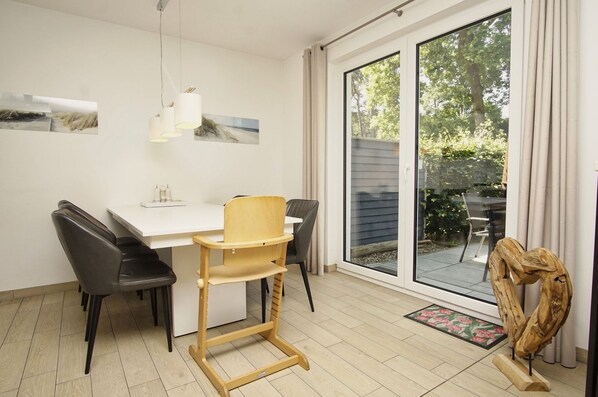 A dining area with a white table, black chairs, a wooden chair, and a view through a glass door to the outside.