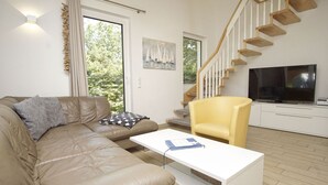 A modern living room with a leather sofa, a yellow armchair, a white coffee table, a flat-screen TV, and a staircase with wooden steps.