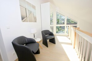 Une chambre moderne avec deux chaises noires, une petite table avec une lampe et une grande fenêtre donnant sur un paysage verdoyant.