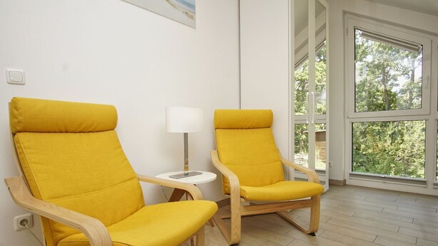 Two yellow armchairs, a small white table with a lamp, and a large window with a view of greenery.
