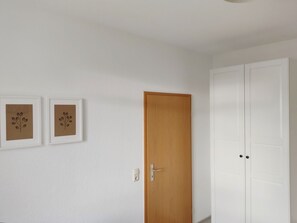 A room with a wooden door, white walls, and two framed pictures.