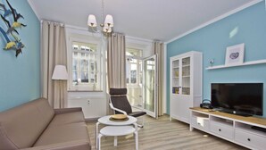A modern living room with a sofa, a chair, a small table, a TV, and a cabinet. - Quiet location in Ostseebad Göhren, veranda, - Villa Möwe FeWo 03 - Villa Möwe (Göhren)