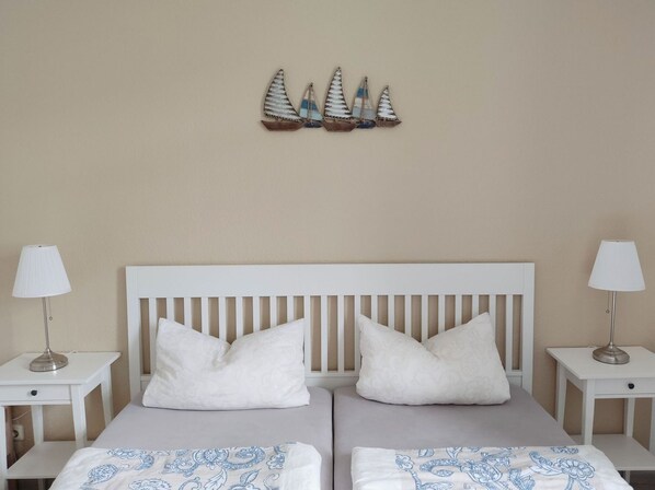 A double bed with two pillows, a white headboard, and a wall decoration of sailboats.
