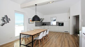 Una cocina moderna con armarios blancos, una mesa de comedor de madera y una lámpara colgante negra.