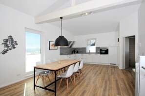Una cocina moderna con armarios blancos, una mesa de comedor de madera y una lámpara colgante negra.