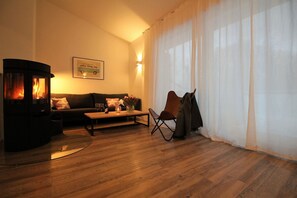 A cozy living room with a wood-burning stove, a sofa, a coffee table, and a chair. - Sealodge - beachfront home with ocean views, access to the pool and sauna - (Göhren)