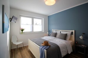 Un dormitorio con cama, una silla, una ventana y una mesita de noche.