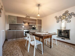 A modern kitchen with a dining area, featuring a central island, white chairs, and a fireplace with decorative plates. - Lovely apartment in villa with private pool, TV, terrace, pets allowed and panoramic view (Cortazzone)
