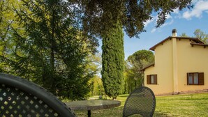 A patio with a round table and two chairs, surrounded by trees and a building with a yellow facade. - Wonderful private villa for 7 guests with WIFI, private pool, TV, terrace and pets allowed (Anghiari)