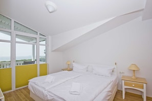 Ein Schlafzimmer mit einem großen Bett, zwei Nachttischen, einem Fenster mit Jalousien und Blick ins Freie.