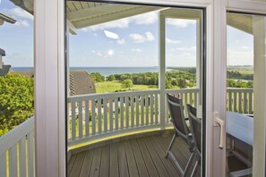 A wooden deck with a white railing, a chair, and a view of a green landscape and water. - With sea view and balcony, use of swimming pool and sauna - sea view apartment 17 - (Göhren)
