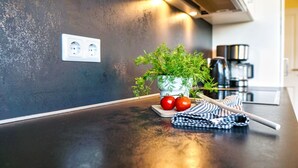 A kitchen counter with a potted plant, tomatoes, and a striped cloth.