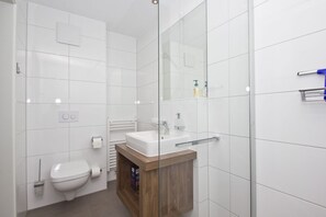 A modern bathroom with a glass shower enclosure, a white toilet, and a wooden vanity with a sink.