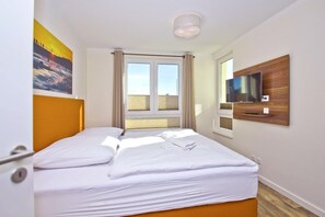 Hotellihuone, jossa on s änky, seinälle asennettu televisio ja ikkuna, jossa on verhot.