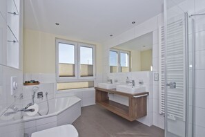 A modern bathroom with a bathtub, two sinks, a large mirror, and a window with blinds.