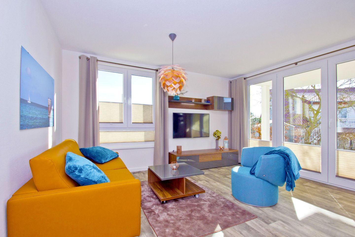 Una sala de estar moderna con un sofá amarillo, un sillón azul y un televisor en la pared.
