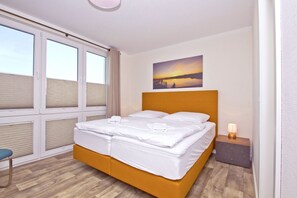 Ein Hotelzimmer mit einem großen Bett, einem Nachttisch, einem Sessel und einem Fenster mit Jalousien.