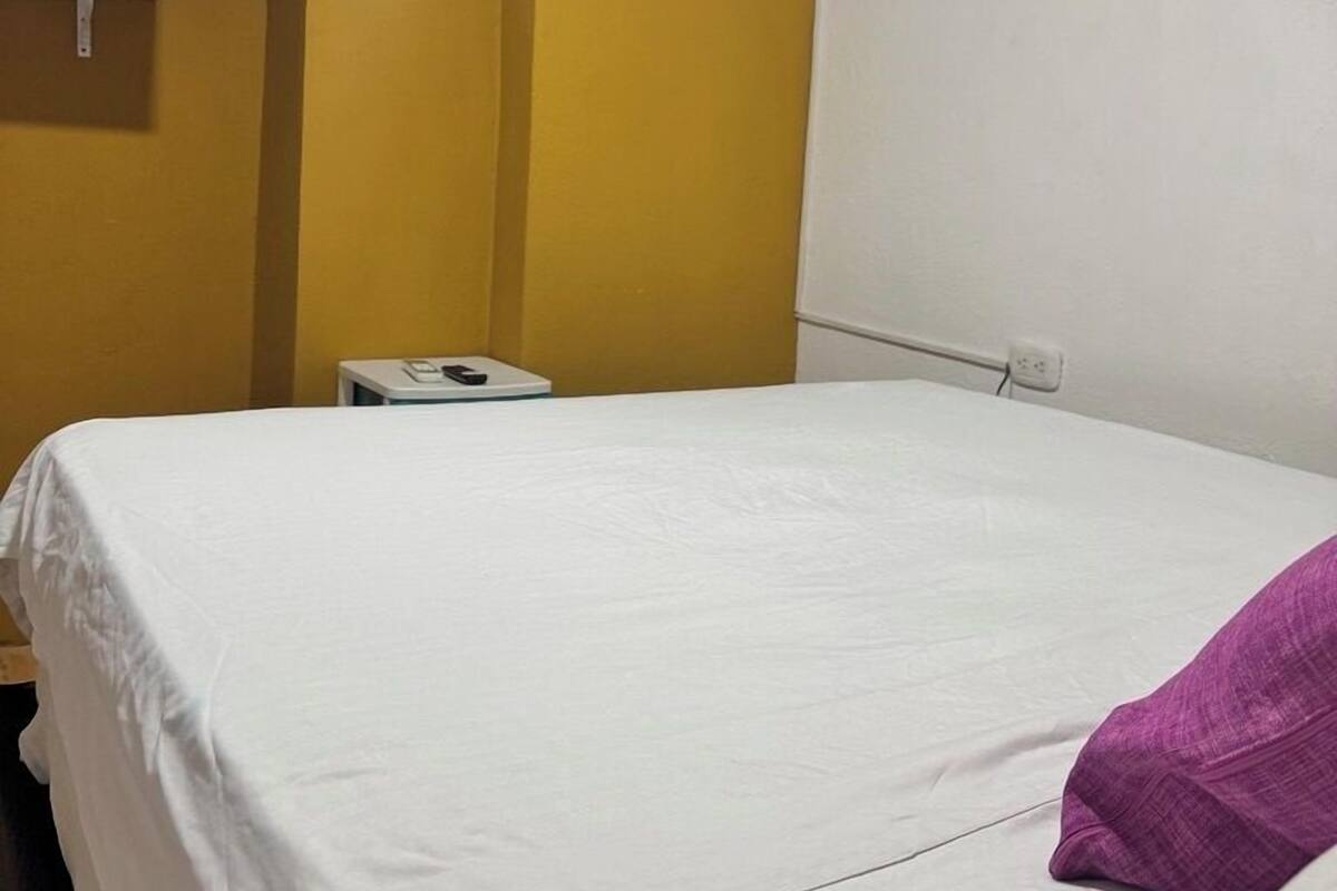 A hotel room with a bed, a TV mounted on the wall, and an air conditioning unit.