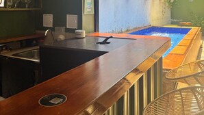 A bar area with a wooden counter, hanging plants, and a view of an outdoor pool. - Hostal Seven Nights Cartagena - Hostel (Cartagena)