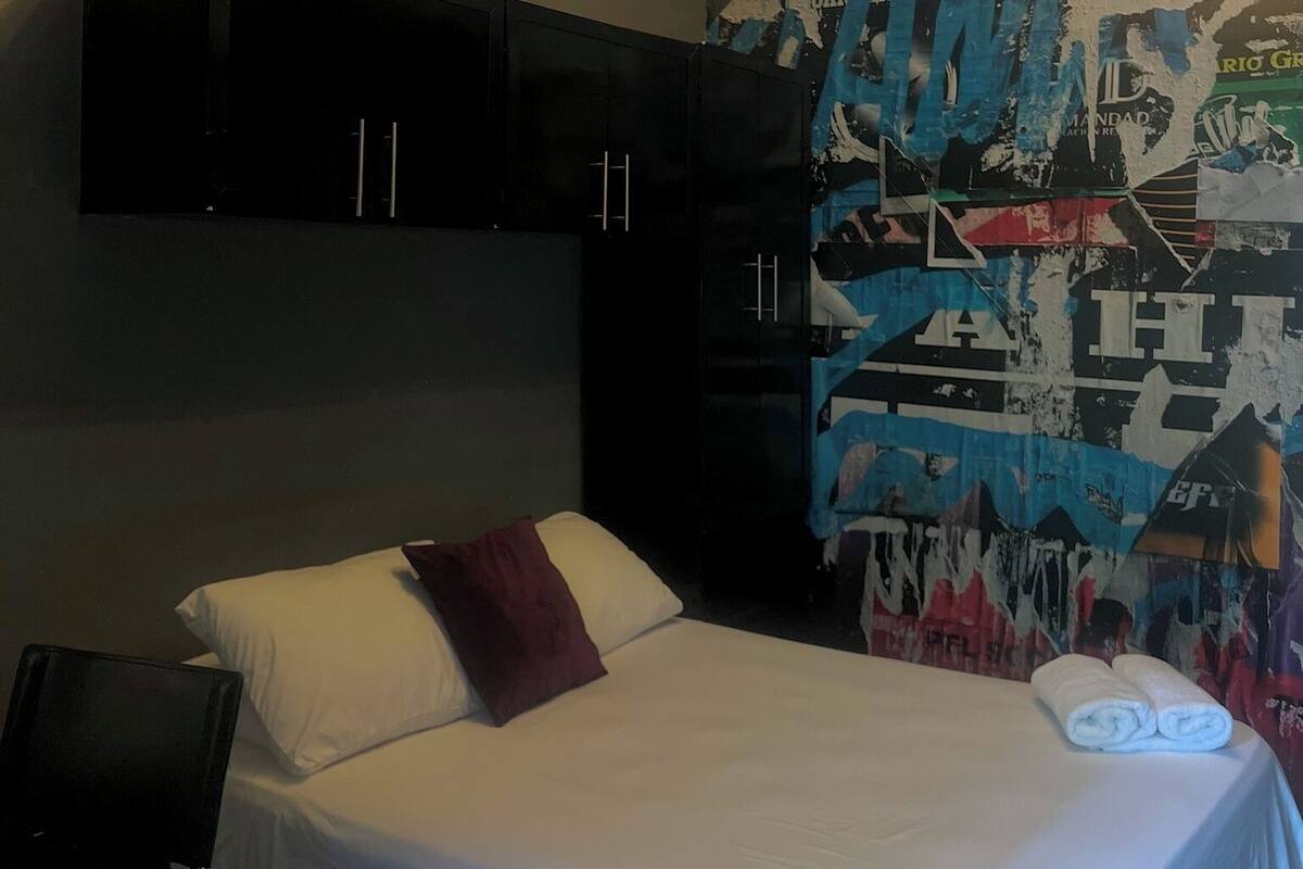 A hotel room with a bed, a black wardrobe, and a wall with a collage of images and text.