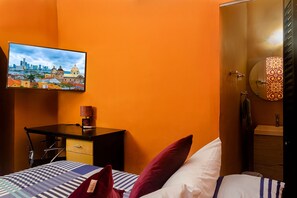A hotel room with a bed, a desk, a chair, a TV mounted on the wall, and a bathroom with a mirror and sink. - Hostal Seven Nights Cartagena - Hostel (Cartagena)