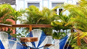A terrace with white and blue wicker chairs, a wooden table, and lush tropical plants. - Hostal Seven Nights Cartagena - Hostel (Cartagena)