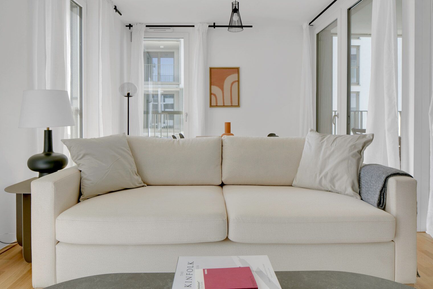 A modern living room with a beige sofa, a floor lamp, and a table with a magazine.