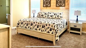 Un dormitorio con cabecera de madera, cama con colcha de estampado selvático, dos mesitas de noche con lámparas y un ventilador de techo.