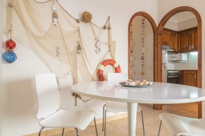 A dining area with a round table, white chairs, and a wall decorated with nautical-themed items.