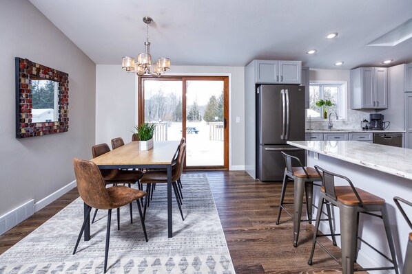 Une cuisine moderne dotée d’un grand îlot central, d’appareils électroménagers en acier inoxydable et d’un coin repas avec une table et des chaises en bois.