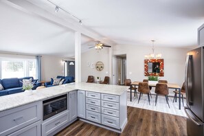 Une cuisine moderne dotée d’un îlot central, d’un four encastré et d’un coin repas avec une table et des chaises en bois.
