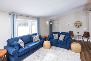 Un salon moderne avec deux canapés bleus, une table basse ronde et une petite table d’appoint.