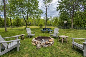 Un jardin avec un foyer, une table de pique-nique et des fauteuils Adirondack.