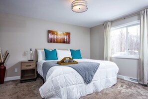 A bedroom with a large bed, a bedside table, a wall-mounted artwork, and a window with curtains.
