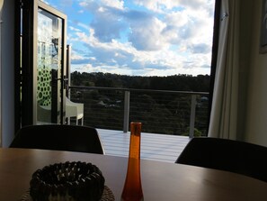A balcony with a table, chairs, and a view of a forested area. - The Origami Apartment. Spacious, private, local views......close to town (Wentworth Falls)