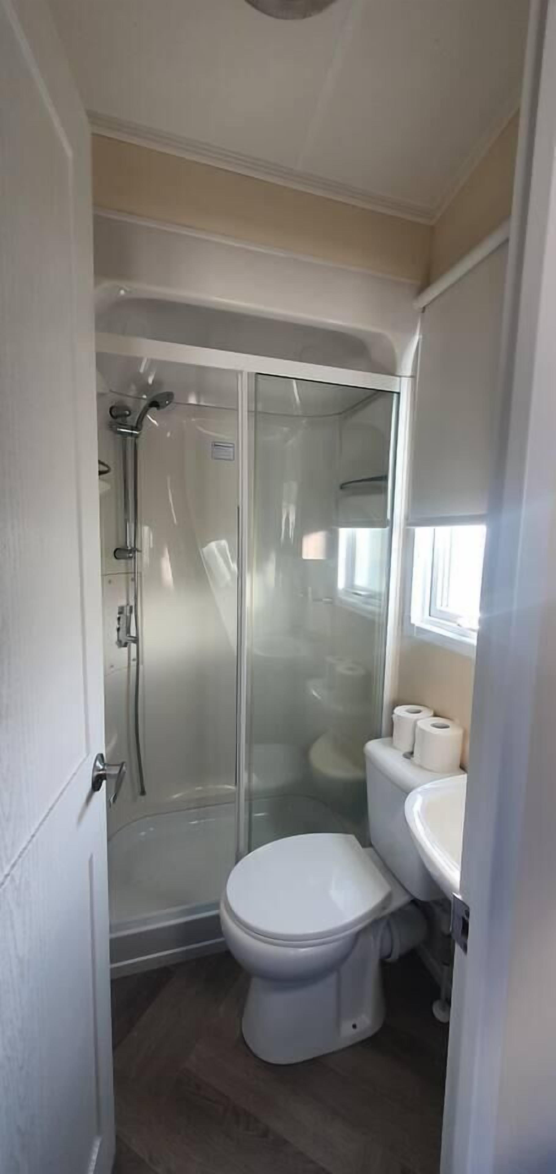 Pieni kylpyhuone, jossa on lasiseinällä varustettu suihku, wc ja pesuallas.
