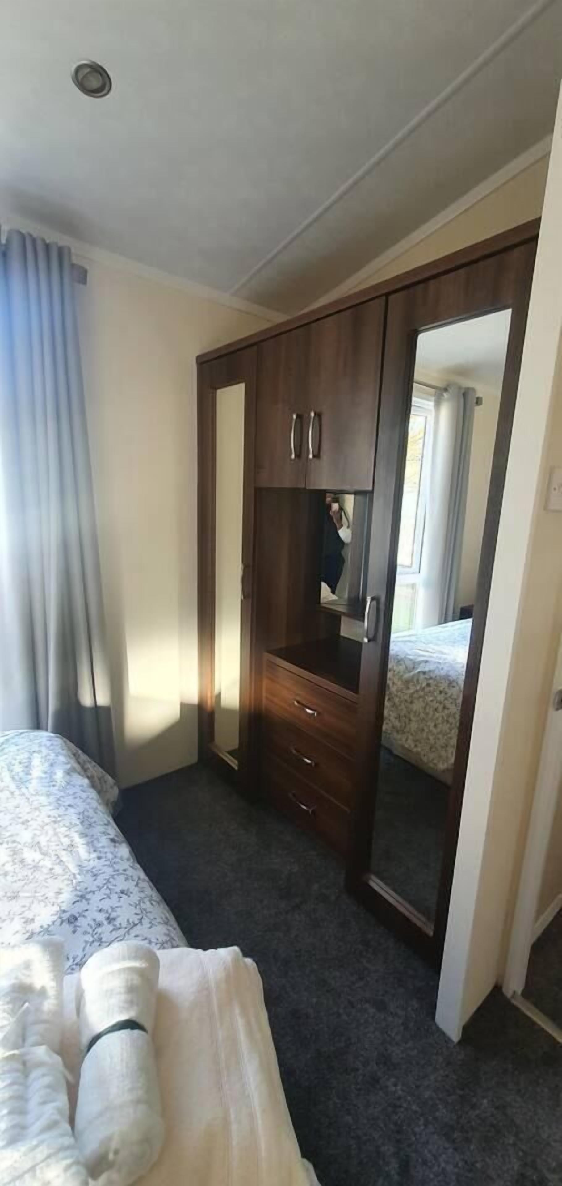 Une chambre d’hôtel avec un lit, une armoire, un miroir et une fenêtre avec des rideaux.