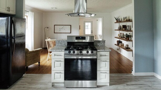 A kitchen with a stainless steel stove, a black refrigerator, white cabinets, and a pendant light.