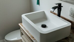 A bathroom with a white sink, a black faucet, and a green towel hanging on the wall.