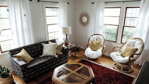A living room with a dark patterned sofa, two white cushioned chairs, a glass coffee table, a red patterned rug, and a wall-mounted mirror.