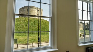 Een kamer met een groot raam met uitzicht op een historische stenen toren en een grasheuvel.
