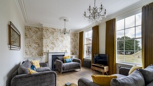 Een woonkamer met twee banken, een open haard, een televisie en een groot raam met gordijnen.