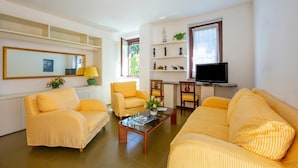 A living room with yellow-striped sofas, a coffee table with flowers, a TV, and a shelf with decorative items. - Appartamento Gaya 2BR with Terrace, Stresa, Italy (Stresa)