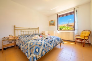 Una camera da letto con un letto, una sedia, un comodino, una finestra vista e un termosifone.