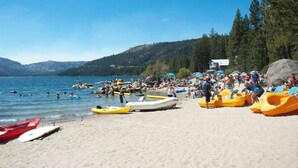 Una playa con kayaks y canoas, un lago y una casa al fondo.