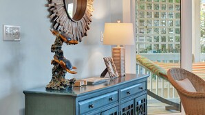 A room with a wooden-framed mirror, a lamp, a wicker chair, and a blue dresser. - Gorgeous Ocean Views, Heated Pool Access (Tybee Island)