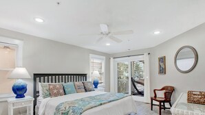 A bedroom with a bed, a ceiling fan, a window with blinds, a chair, and a wicker table. - Gorgeous Ocean Views, Heated Pool Access (Tybee Island)