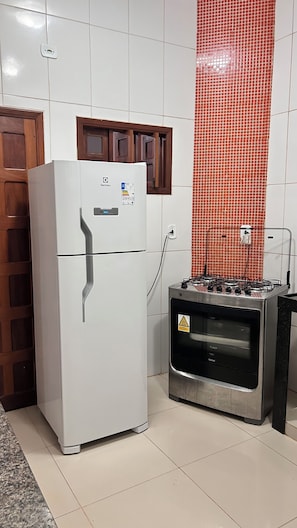 Eine Küche mit einem weißen Kühlschrank, einem Gasherd und einer gefliesten Spritzschutzwand.