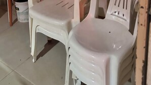 Deux chaises en plastique blanc, un balai et une pelle appuyés contre un mur.