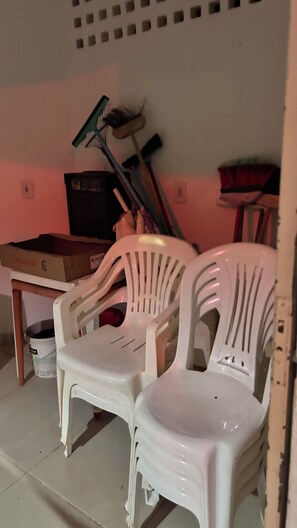Twee witte plastic stoelen, een bezem en een blikvanger leunen tegen een muur.